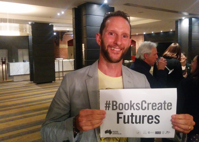 A photo of Matt Shanks holding a "Books Create Futures" sign